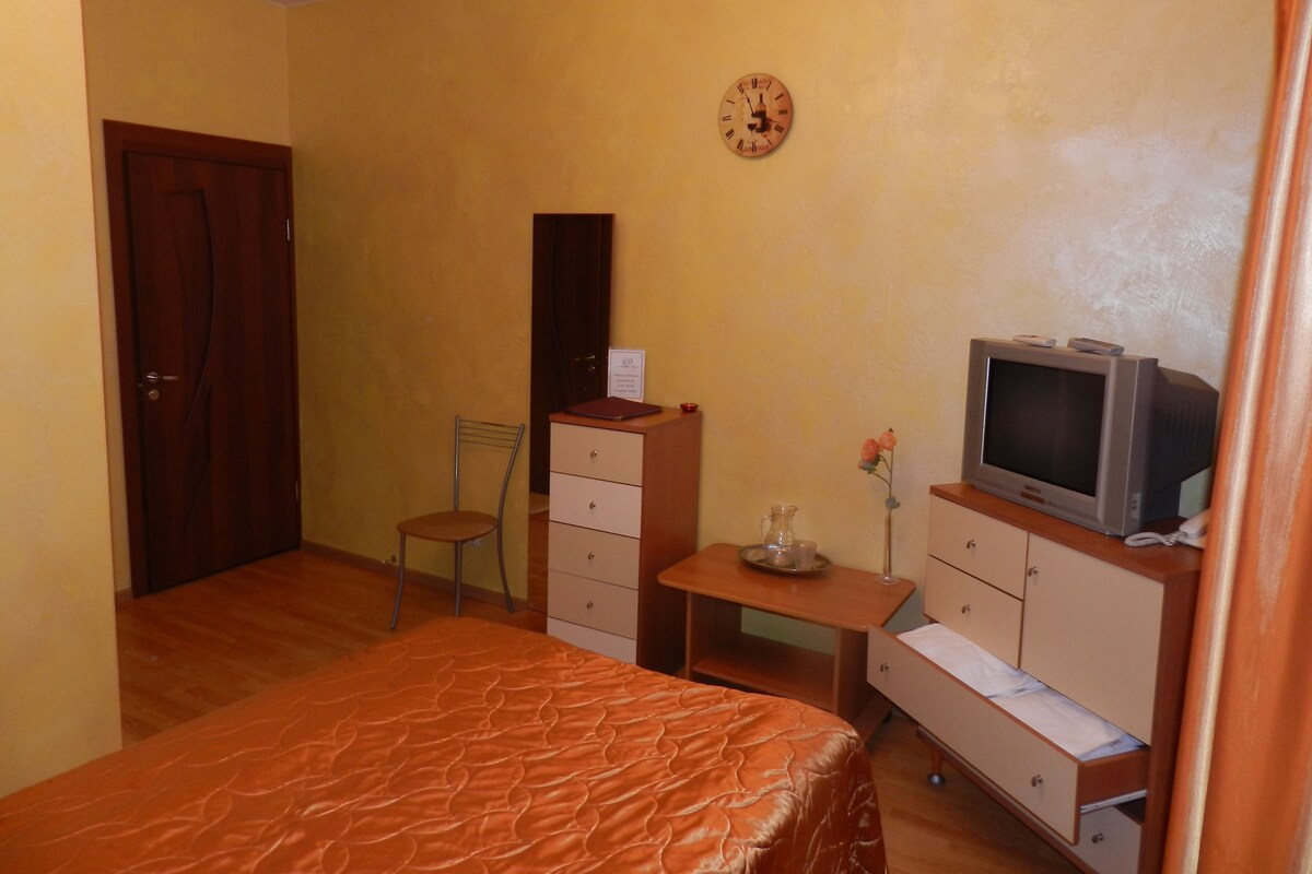 A bedroom with a bed, a dresser, a chair, a small table with a vase, and a television on a cabinet.