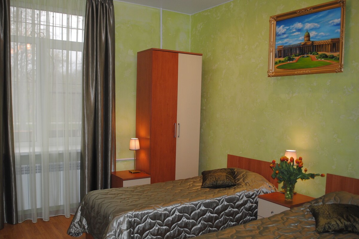 A hotel room with a bed, a wardrobe, a desk with a lamp, a television, and a painting on the wall.