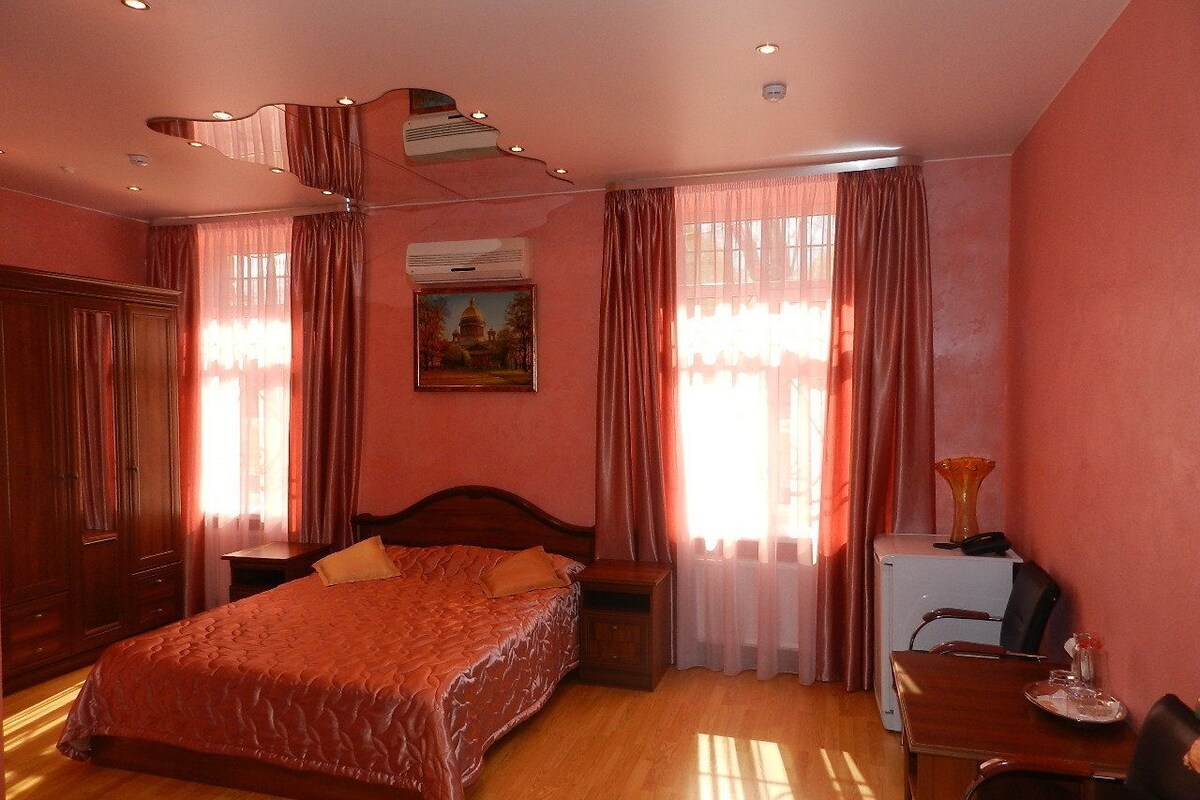 A bedroom with a large bed, a desk with a chair, a small table, and a radiator.