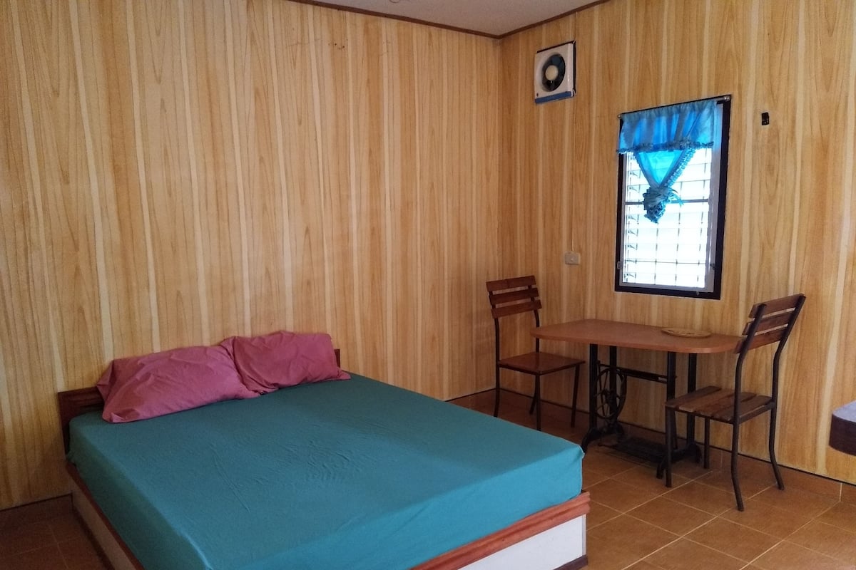 Una habitación con cama, dos sillas, una mesita y una ventana con cortinas.
