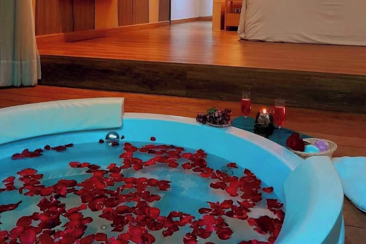 Habitación de hotel con una cama grande, una zona de estar con vistas y una bañera con pétalos de rosa.