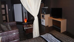 A modern hotel room with a bed, a TV, a minibar, and a seating area with a sofa and a coffee table. - NUDA by H-Seven - Adults Only (Yokohama)
