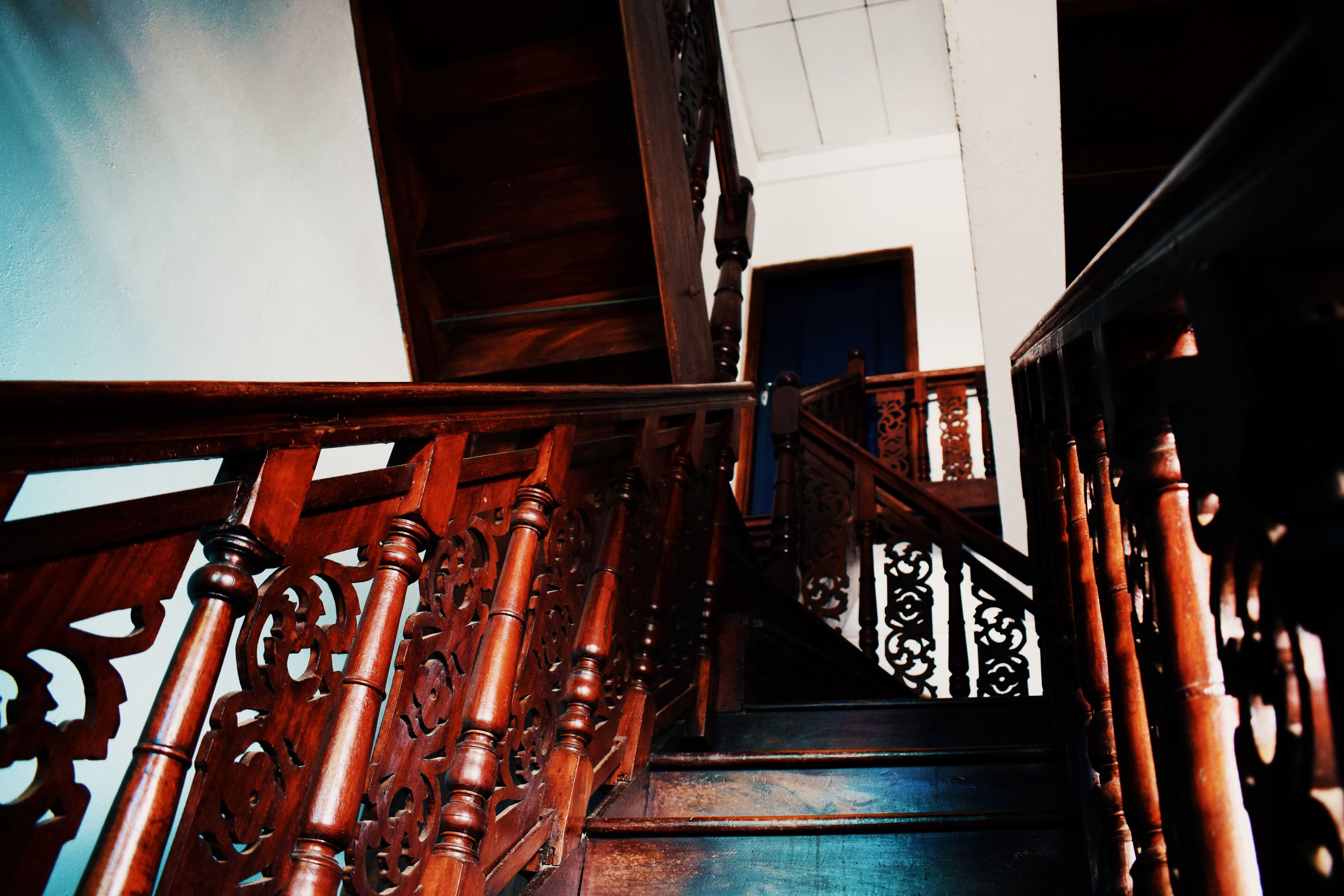 A wooden staircase with intricate railings and a blue carpet.