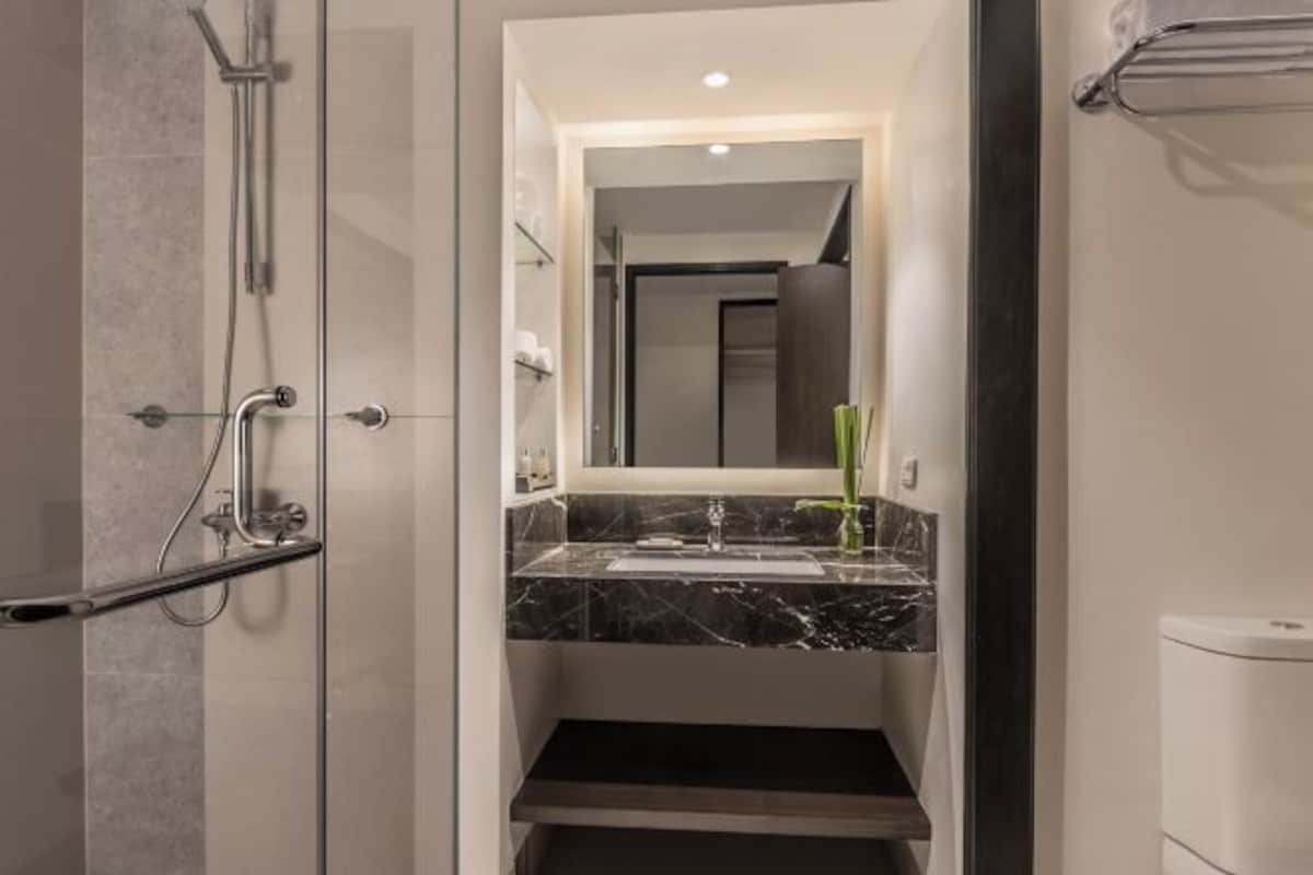 Un baño moderno con cabina de ducha de vidrio, encimera de mármol y un espejo grande.