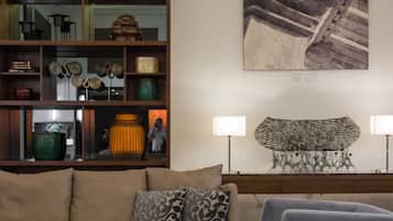 A living room with a sofa, armchairs, a glass coffee table, a wooden bookshelf, and a large abstract painting on the wall.