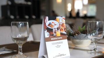 A breakfast buffet sign on a table with two empty wine glasses.