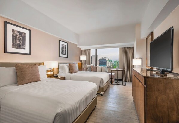 A hotel room with two beds, a desk, a TV, and framed pictures on the wall. - Seda Ayala Center Cebu City (Cebu City)
