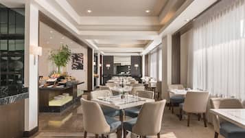 Un comedor moderno de hotel con una larga mesa, numerosas sillas y una estación de bufé.