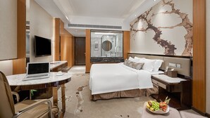 A modern hotel room with a large bed, a desk with a laptop, a flat-screen TV, and a fruit bowl on the side table. - Guangzhou Manguo International Hotel (Guangzhou)