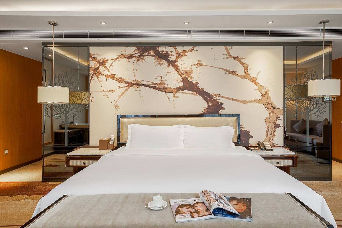 Una habitación de hotel moderna con una cama grande, mesitas de noche, un espejo y un elemento decorativo en la pared.