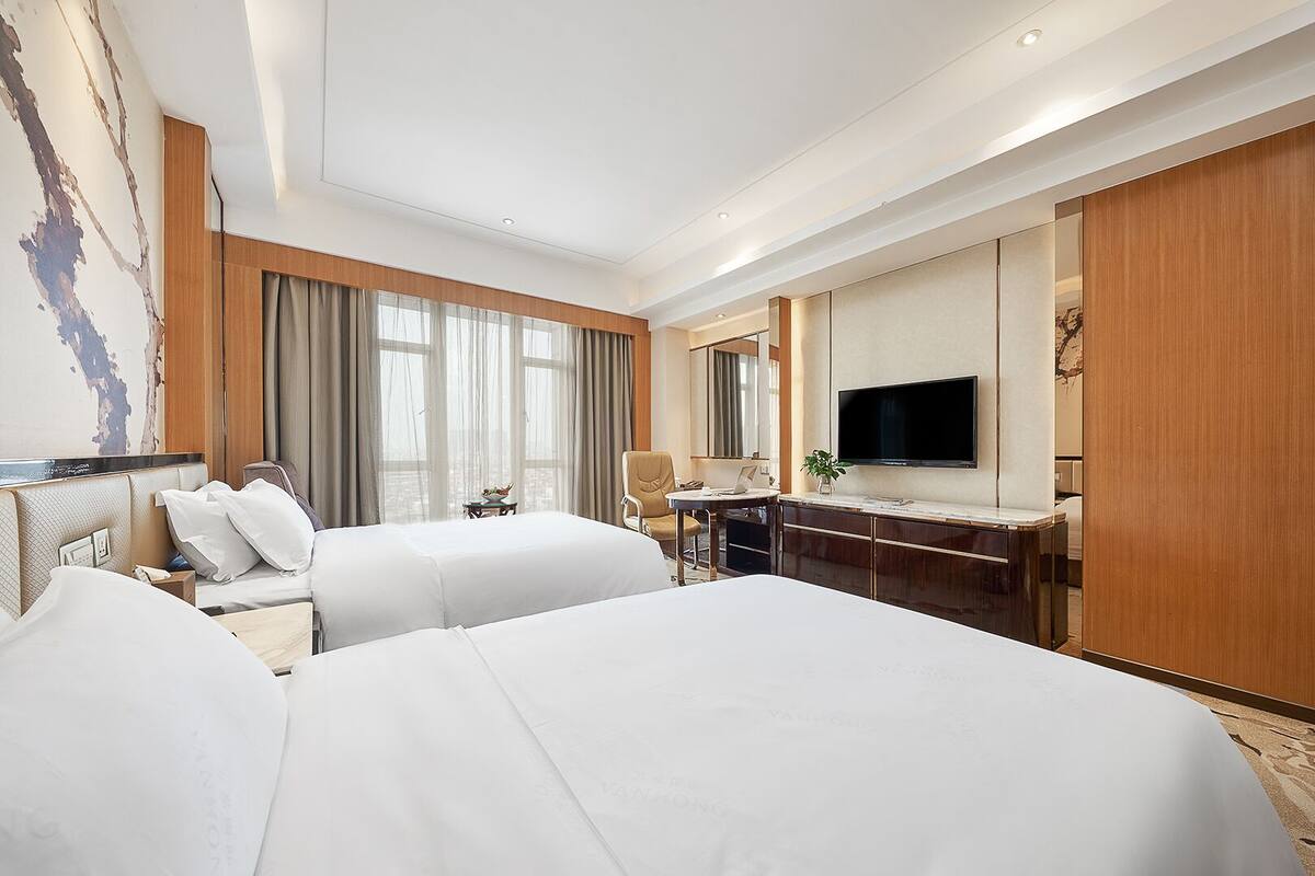 Habitación de hotel con dos camas, un escritorio, un televisor y un ventanal con cortinas.