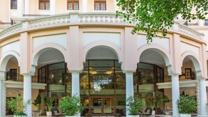A hotel entrance with a central glass door, white columns, and potted plants. - DLF Club 5 (Gurugram)