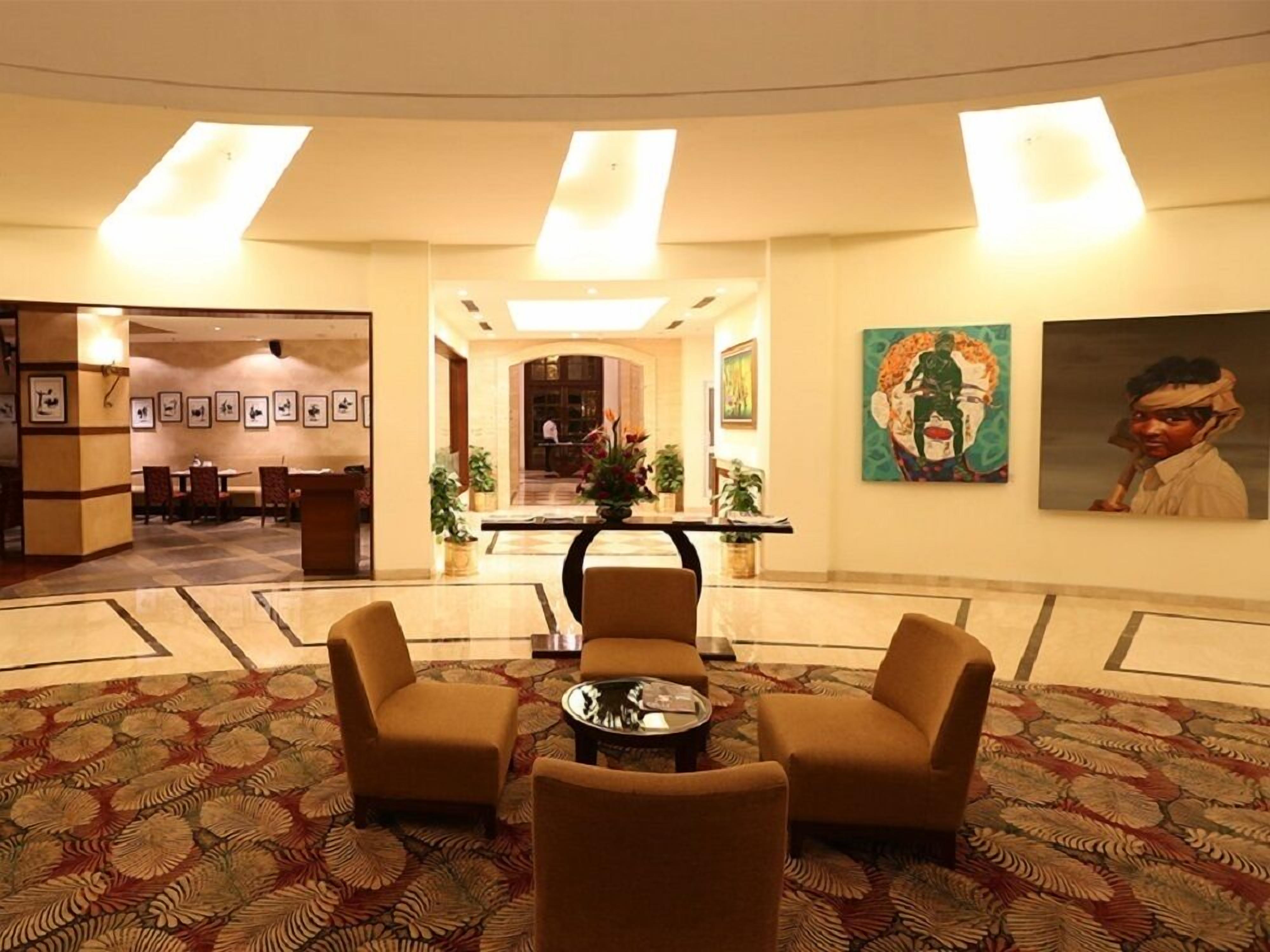 A hotel lobby with a reception desk, seating area with armchairs, a coffee table, and artwork on the walls.