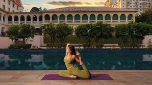 A person performing yoga on a mat by a pool with a building in the background. - DLF Club 5 (Gurugram)