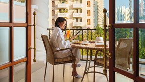 A person sitting at a round table with a balcony view, holding a drink and a book. - DLF Club 5 (Gurugram)