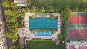 An aerial view of a resort with a swimming pool, tennis courts, and lush greenery. - DLF Club 5 (Gurugram)