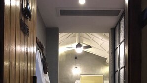 Un couloir avec une porte en bois, une serviette blanche suspendue, un ventilateur de plafond et une baignoire près d’une fenêtre.