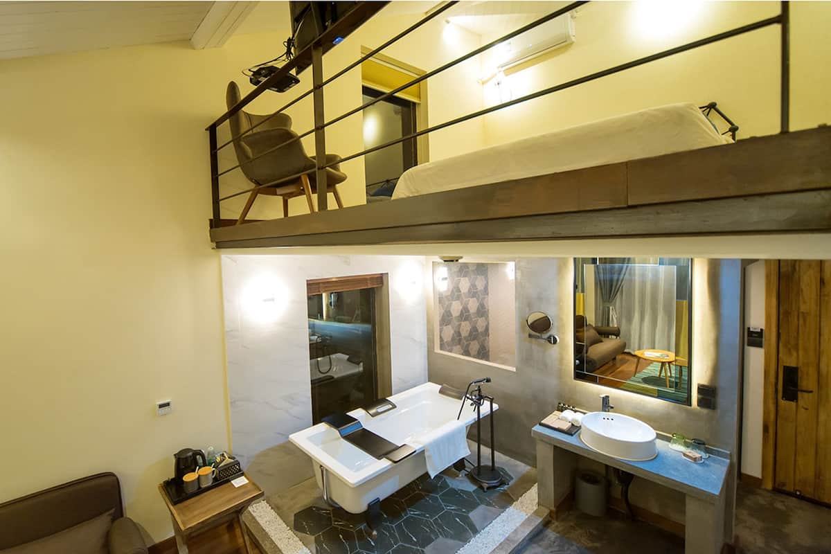 A modern bathroom with a bathtub, a sink, and a mirror. There is a wooden bench and a small table with toiletries.