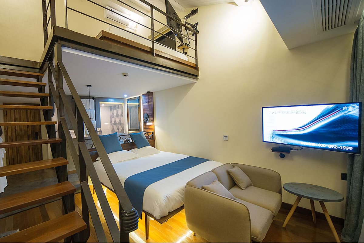 A bedroom with a bed, a TV, a sofa, and a staircase.