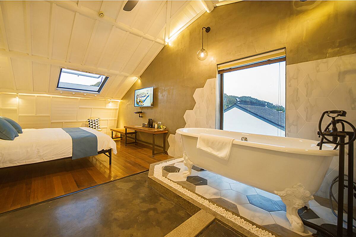 A bedroom with a bed, a desk, and a large window.