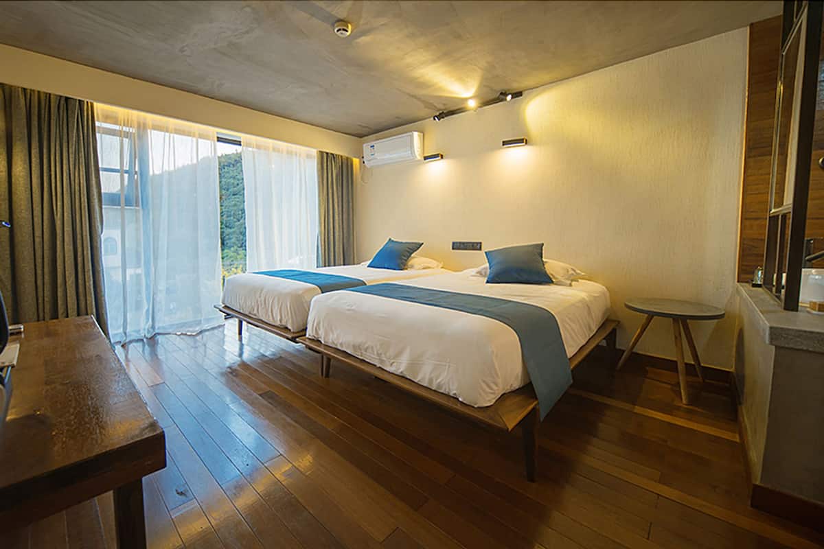 A hotel room with two beds, a desk, a chair, a small table, and a view of the outdoors.