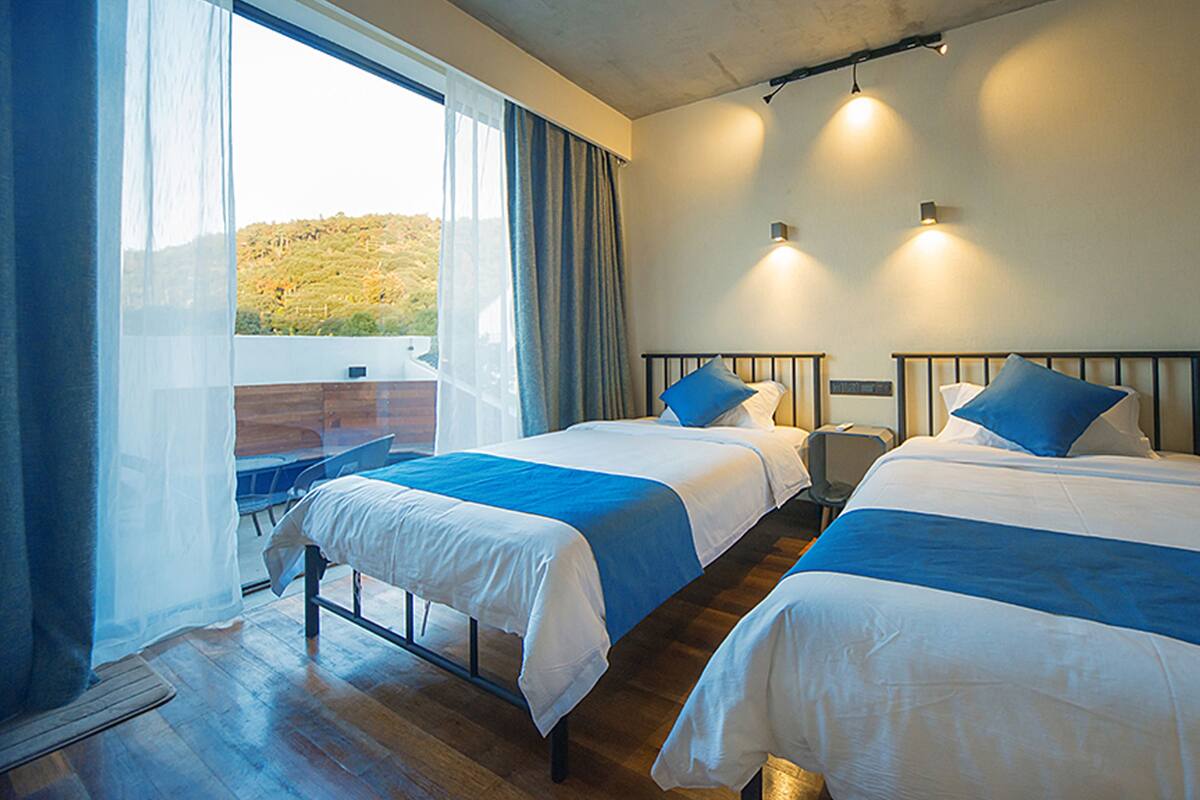 A hotel room with two beds, a balcony, and a view of the outdoors.