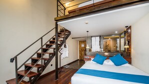 Une chambre d’hôtel avec un escalier en bois, un grand lit avec une literie bleue et blanche, une table de chevet en bois et un miroir au-dessus du lit.