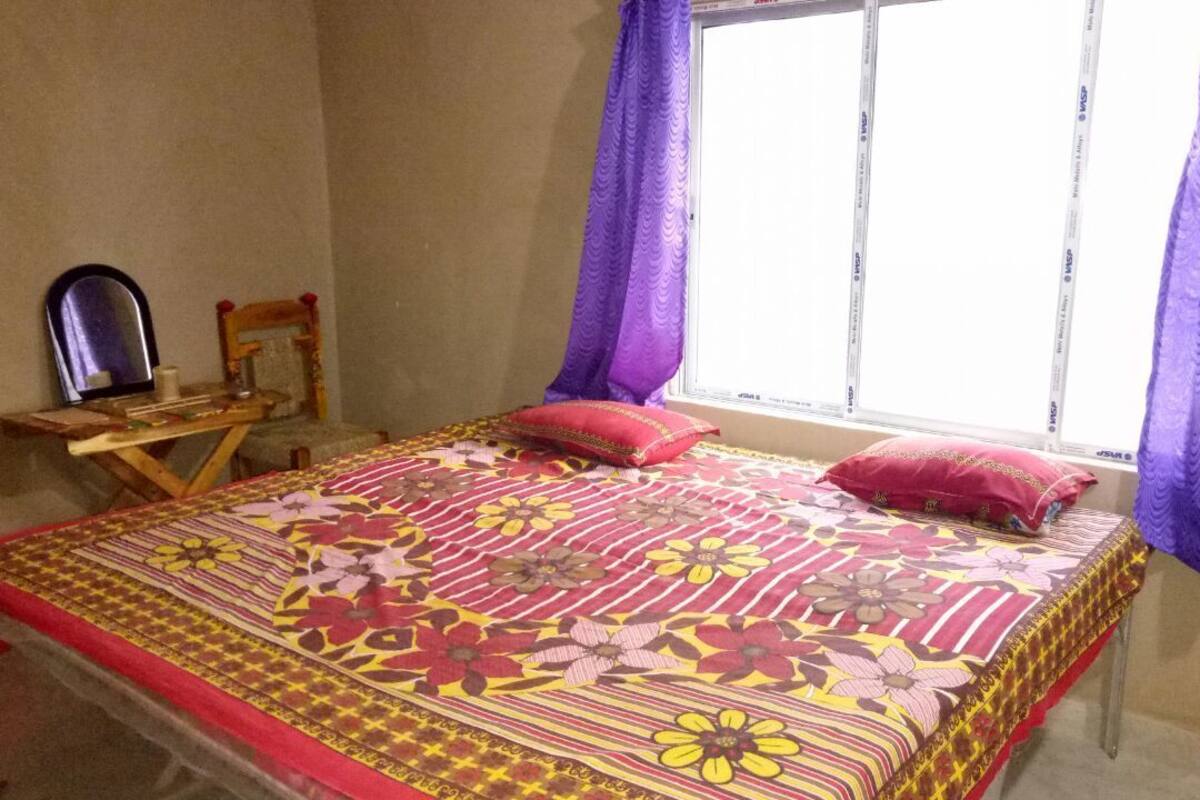 A bedroom with a bed, a wooden chair, a small table, and a window with purple curtains.