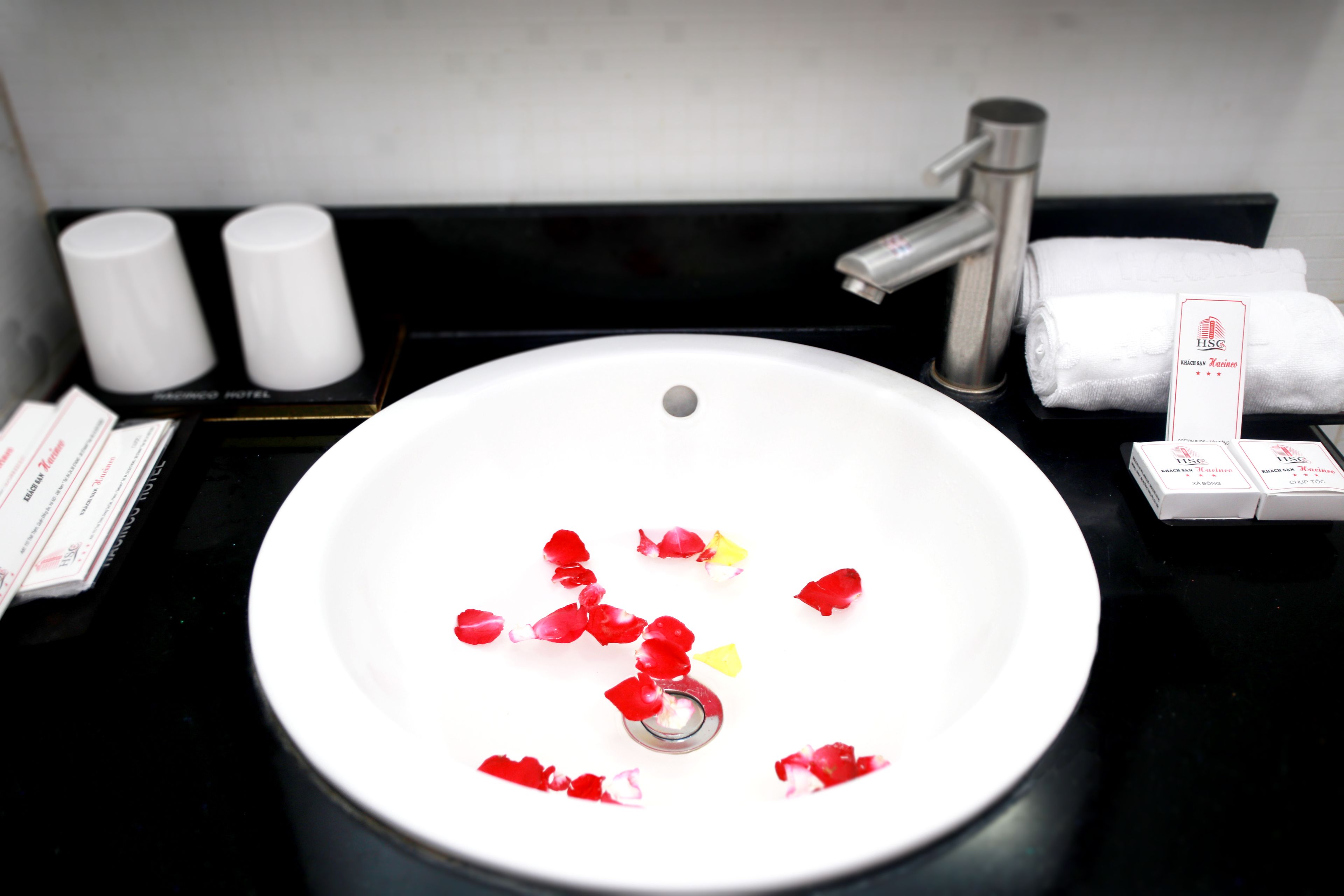 A bathroom sink with rose petals, toiletries, and a towel rack.
