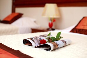 A neatly made bed with a rolled-up magazine and a red rose on the bedspread. - Hacinco Hotel (Hanoi)
