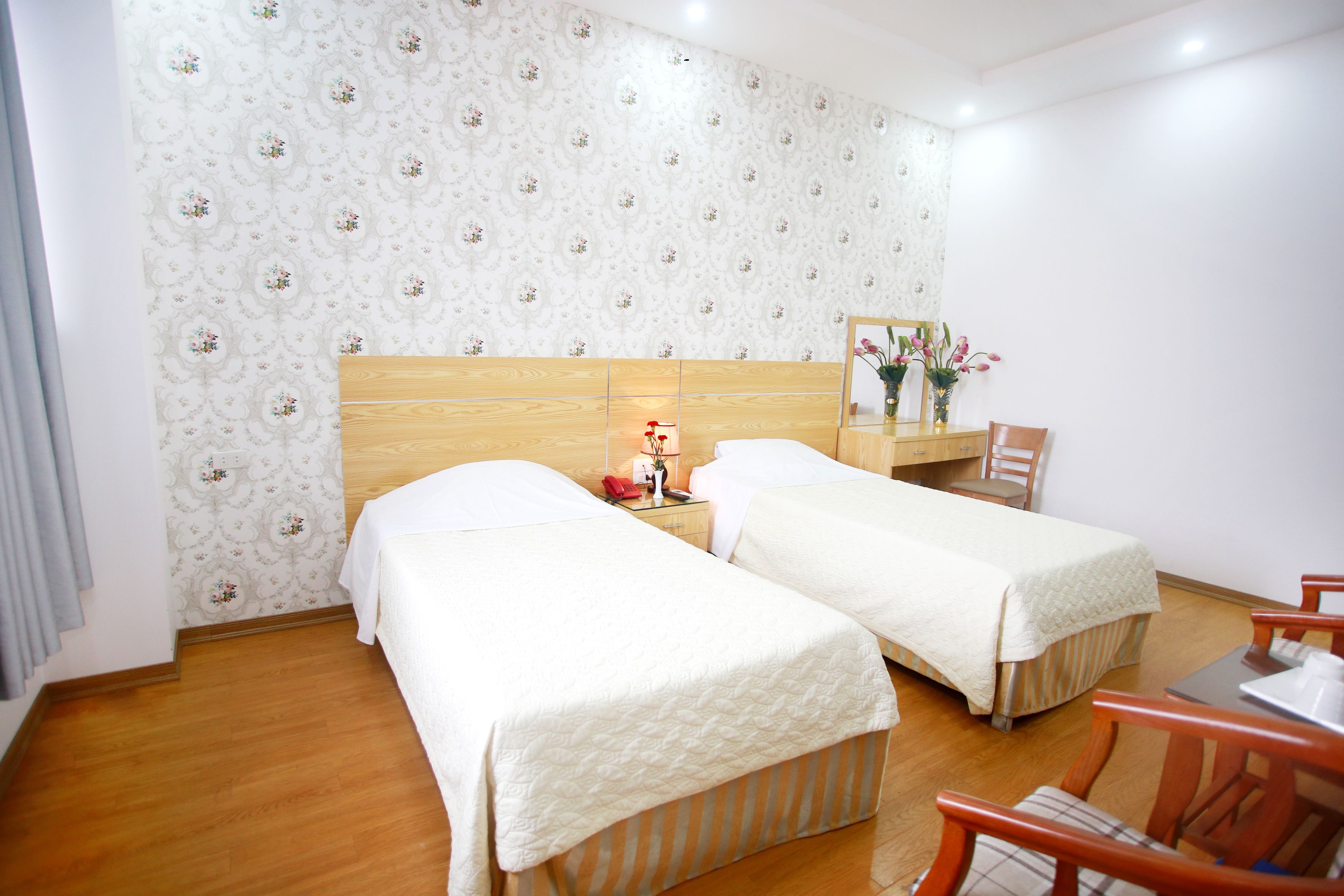 Une chambre d’hôtel avec deux lits, une tête de lit en bois, une table de chevet avec une lampe, un miroir et une chaise.