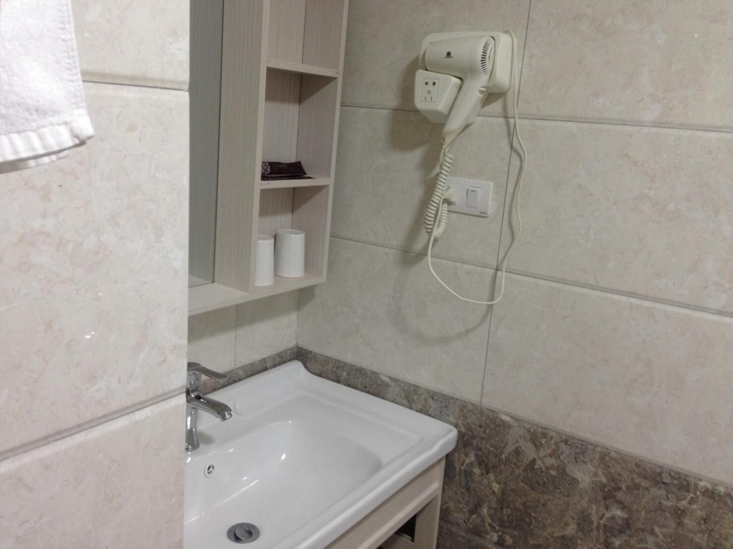 A bathroom with a white sink, a towel rack, a hairdryer on the wall, and a shelf with toiletries.