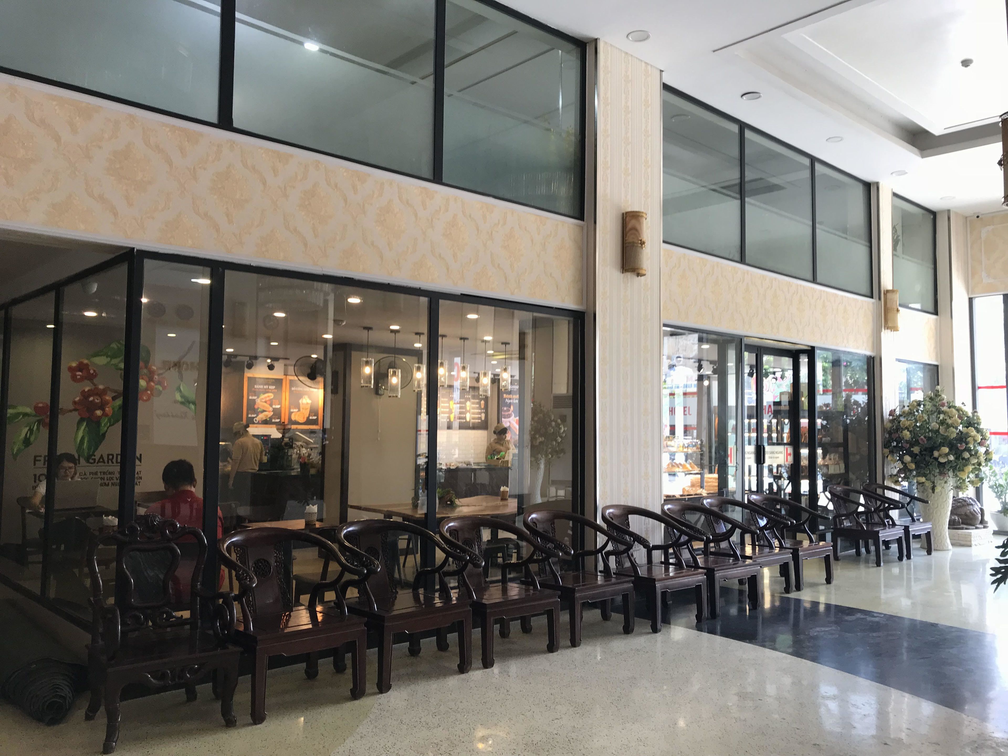 A spacious indoor area with a seating area featuring wooden chairs and tables, large windows, and a modern interior design.