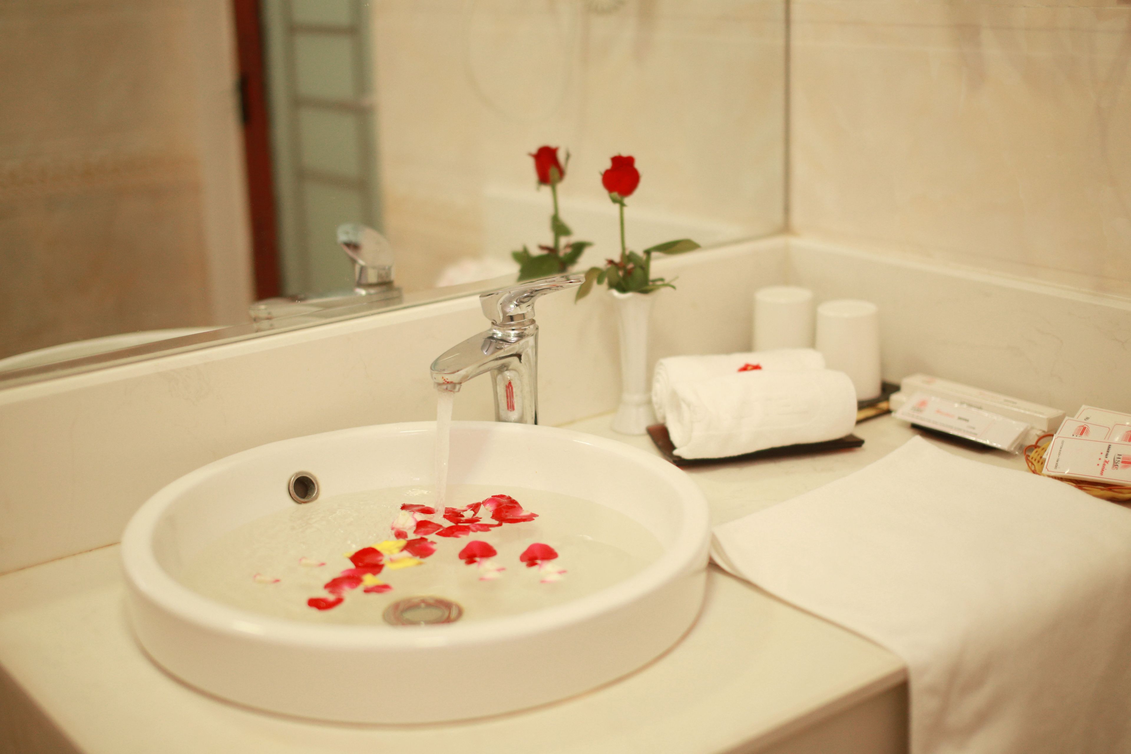A bathroom with a sink, a mirror, a towel rack, and a vase with flowers.