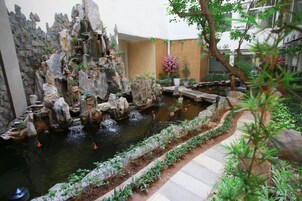 Jardim de pedras com lago, muros de pedra e diversas plantas.