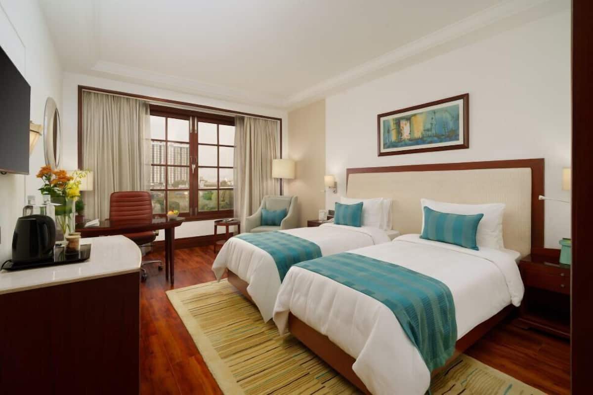A hotel room with two beds, a desk, a chair, a TV, and a window with curtains.