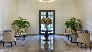 A spacious lobby with a polished marble floor, two sofas, a central table with a vase of flowers, and potted plants. - DLF Club 3 (Gurugram)