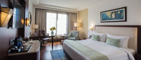 Une chambre d’hôtel avec un grand lit, un bureau avec une lampe, une chaise et un tableau au mur.