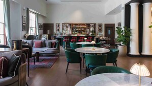A bar area with green chairs and a bar counter. There are multiple framed pictures on the walls. - DLF Club 3 (Gurugram)