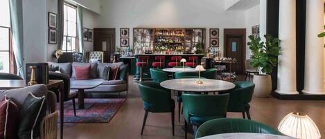 A bar area with green chairs and a bar counter. There are multiple framed pictures on the walls.