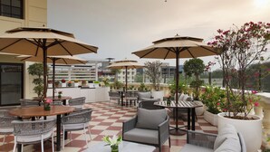 An outdoor patio area with checkered flooring, multiple seating arrangements including tables and chairs, and large umbrellas providing shade. - DLF Club 3 (Gurugram)