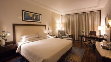 A hotel room with a large bed, a desk, a chair, a lamp, and a painting on the wall.