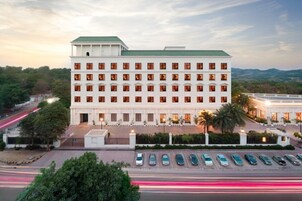 A large, multi-story hotel with a symmetrical facade, numerous windows, and a parking lot with several cars.