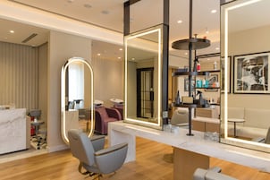 Een modern ingerichte salon met een marmeren receptiebalie, een zithoek en een grote spiegel met ingebouwde verlichting.