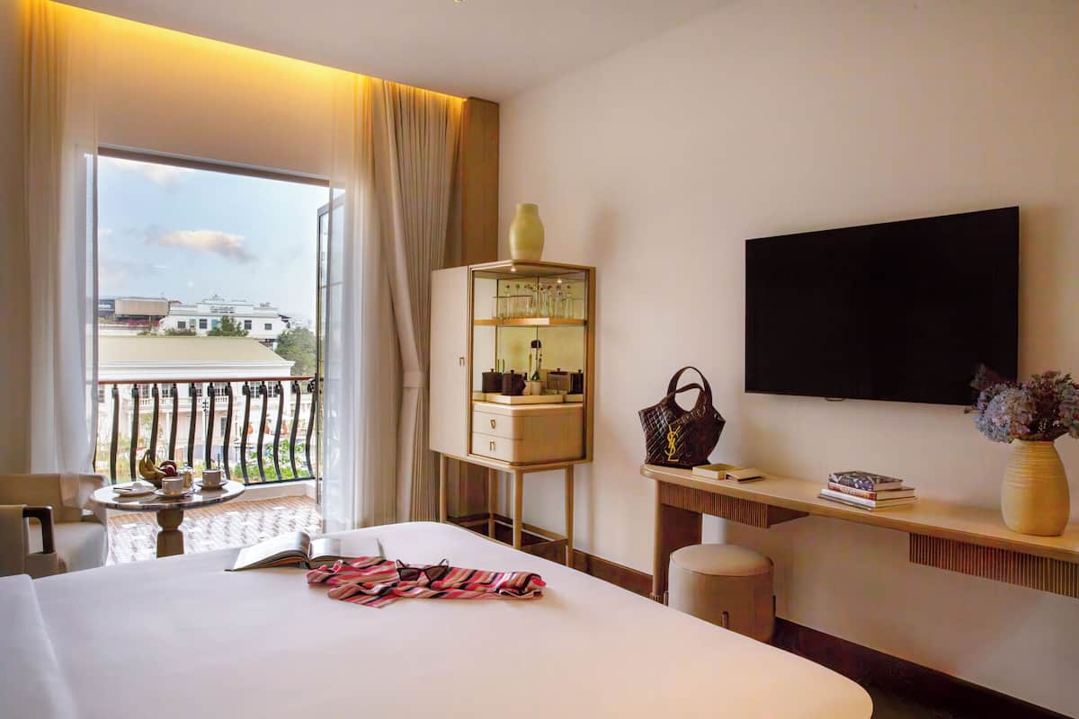 Una habitación de hotel con una cama, un escritorio, un televisor, una ventana con cortinas y un balcón.