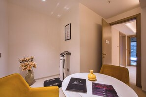 A hotel room with a round table, a yellow chair, a vase with flowers, a massage chair, and a framed picture on the wall. - DLF Club 4 (Gurugram)