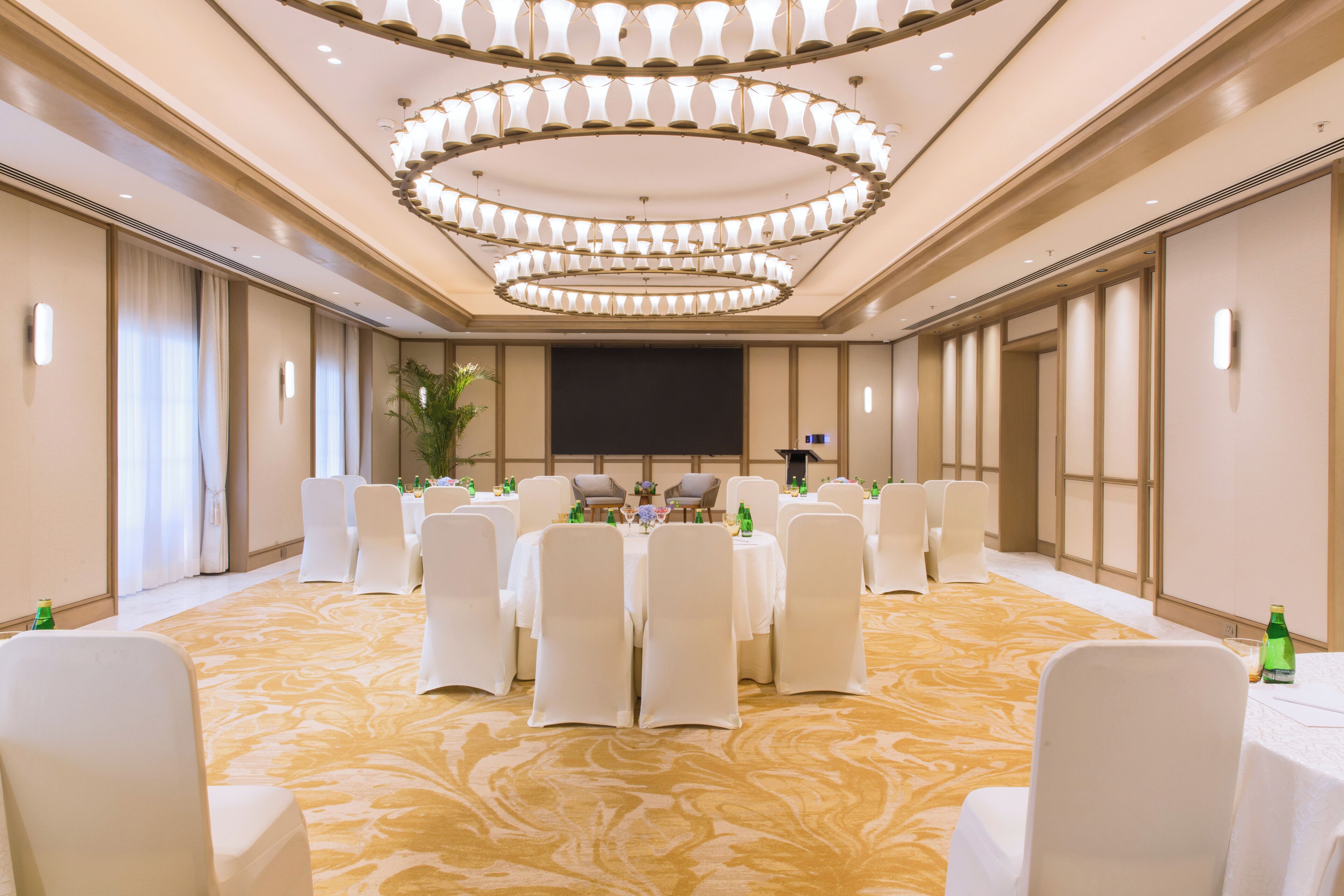A conference room with round tables, white chairs, and a large screen.