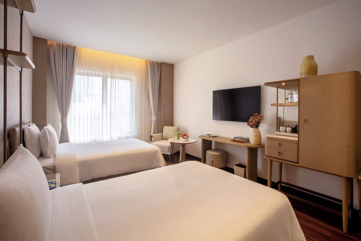Una habitación de hotel con dos camas, un escritorio, una silla, un televisor y un armario.