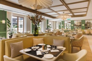 Een restaurant met zitjes, gedekte tafels en een grote vaas met bloemen.