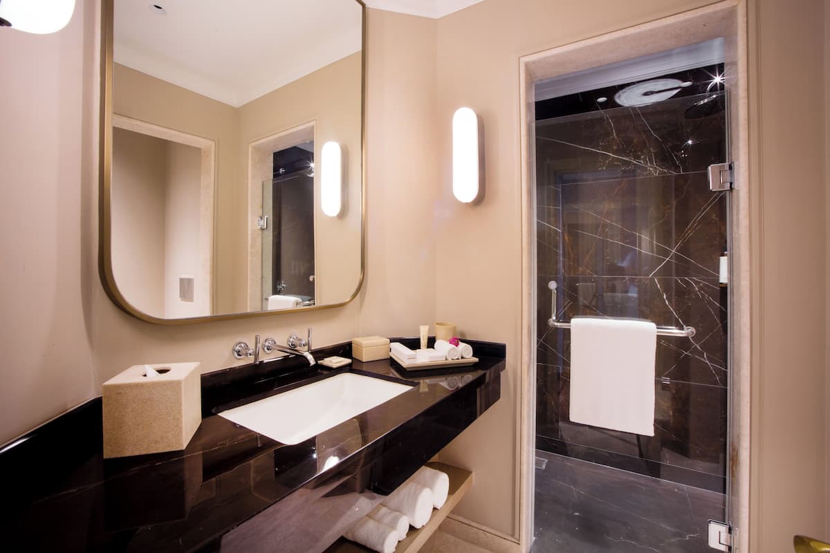 Un baño moderno con un espejo grande, un lavamanos, cabina de ducha con mampara de vidrio y un perchero para toallas.